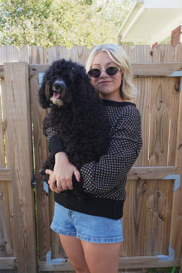 Woman holding a black dog outdoors with a wooden fence and trees in the background