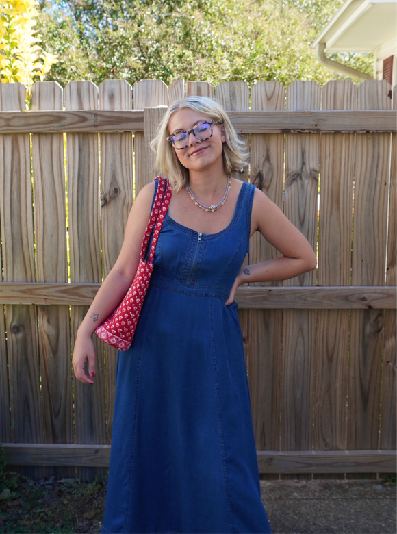 Woman in a blue dress holding a red polka dot bag against a wooden fence.