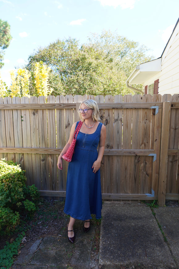 Woman in a blue dress standing in front of a wooden fence with trees in the background