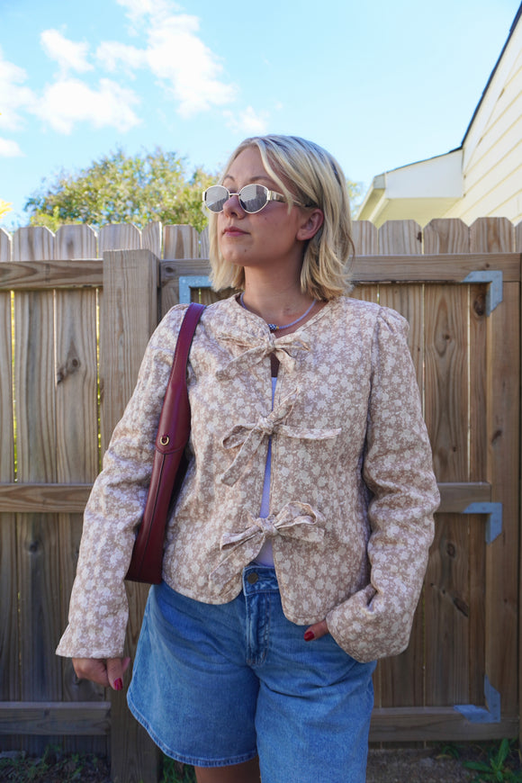 Person wearing a floral jacket and blue shorts standing in front of a wooden fence.