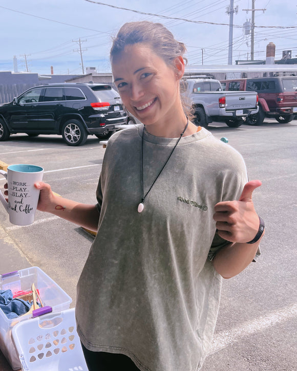 Woman holding a coffee cup and wearing a green good vibes t-shirt in a parking lot