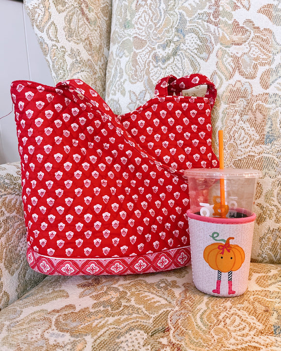 Red patterned tote bag and a cup with a pumpkin design on a textured surface.