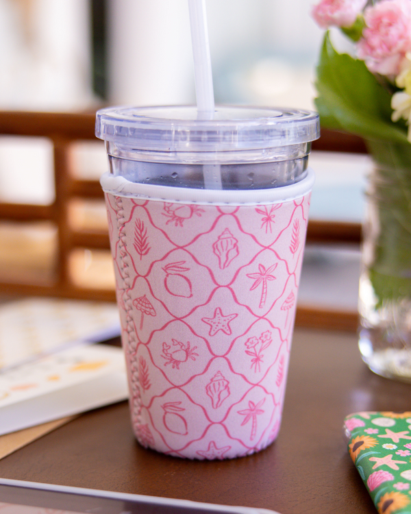 Pink patterned tumbler on a table with a tablet and flowers in the background