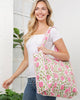 Woman holding a pink and green patterned tote bag against a white wall.