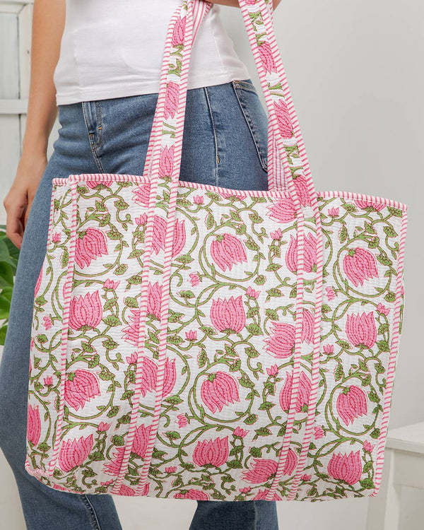 Person holding a floral patterned tote bag with pink flowers and green leaves.
