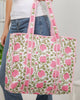 Person holding a floral patterned tote bag with pink flowers and green leaves.