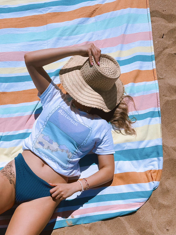 Person lounging on a colorful striped towel on sand