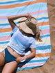 Person lounging on a colorful striped towel on sand
