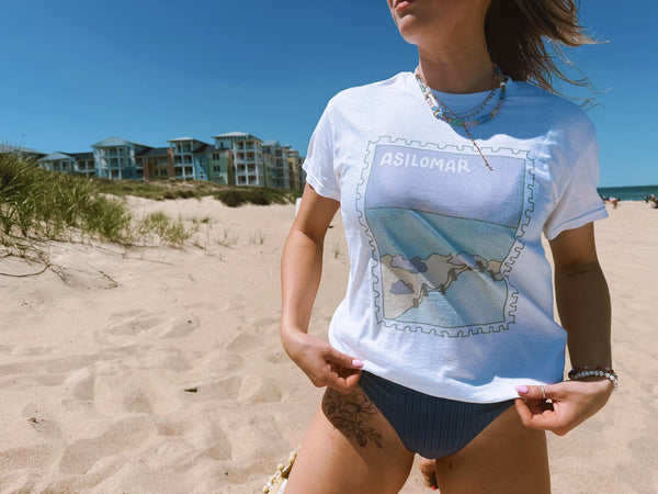 Person wearing a white t-shirt with a graphic design on a beach