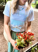 Person wearing a t-shirt with a graphic design, holding flowers outdoors.