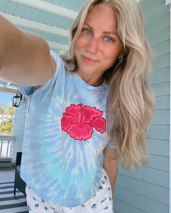 Woman wearing a tie-dye shirt with a pink flower design outdoors.