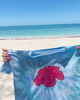 Tie-dye shirt with a pink flower design held up against a beach background