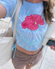 Person wearing a blue tie-dye crop top with a pink floral design, standing on a beach.