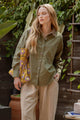 Woman wearing a green shirt and beige pants holding a colorful bag outdoors.