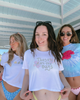 Three women standing together, wearing casual summer clothing with graphic designs.