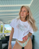 Woman wearing a white t-shirt with floral text and colorful underwear on a porch.