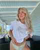 Woman wearing a white t-shirt with floral text and colorful underwear on a porch.