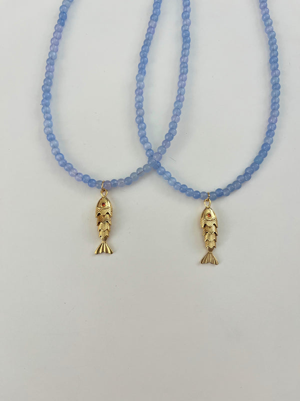 Two blue beaded necklaces with gold fish pendants on a light gray background