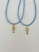 Two blue beaded necklaces with gold fish pendants on a light gray background