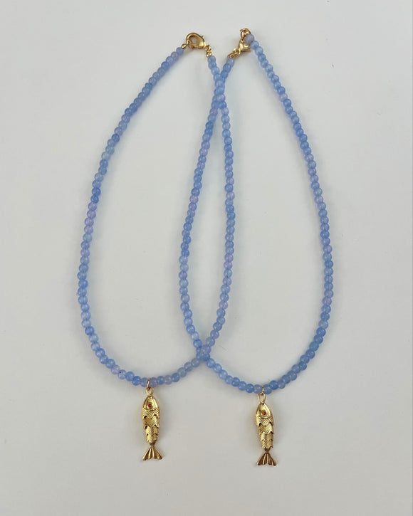 Two blue beaded necklaces with gold fish pendants on a light gray background
