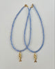 Two blue beaded necklaces with gold fish pendants on a light gray background