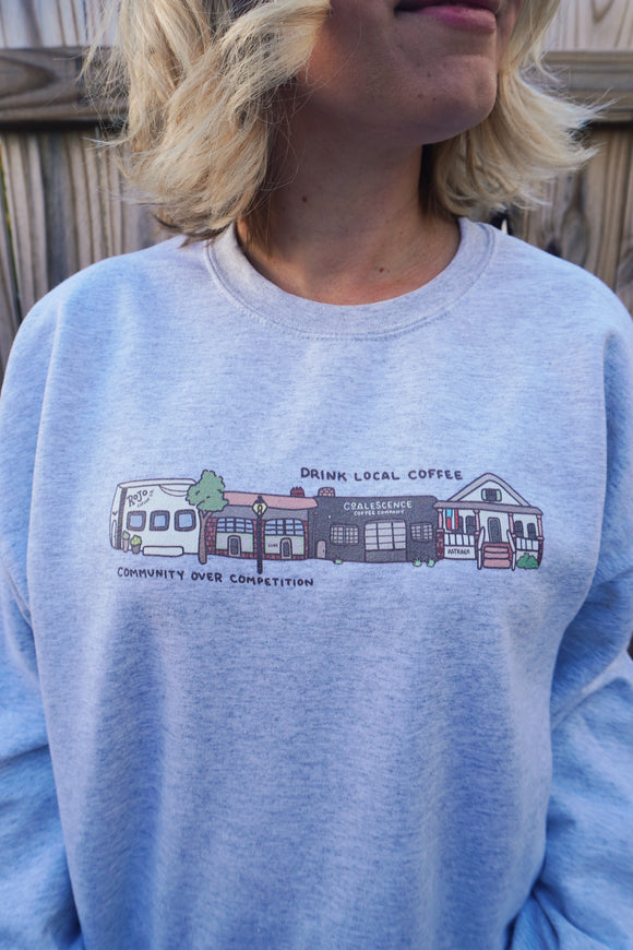 Light grey sweatshirt with a graphic design of buildings and text on a wooden background