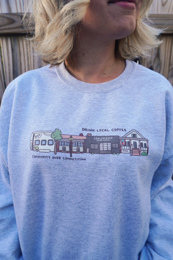 Light grey sweatshirt with a graphic design of buildings and text on a wooden background