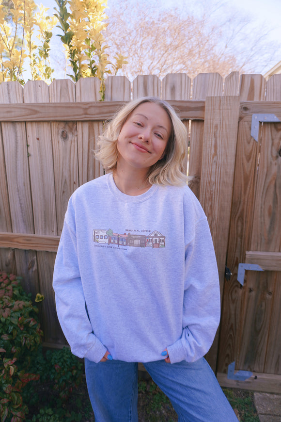 Person wearing a light blue sweatshirt with a graphic design, standing in front of a wooden fence.