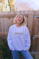 Person wearing a light blue sweatshirt with a graphic design, standing in front of a wooden fence.