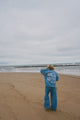Person in blue outfit standing on a beach looking at the ocean