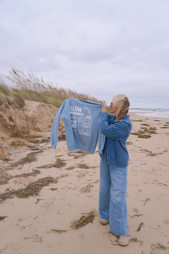Person holding a blue sweater with text on a beach