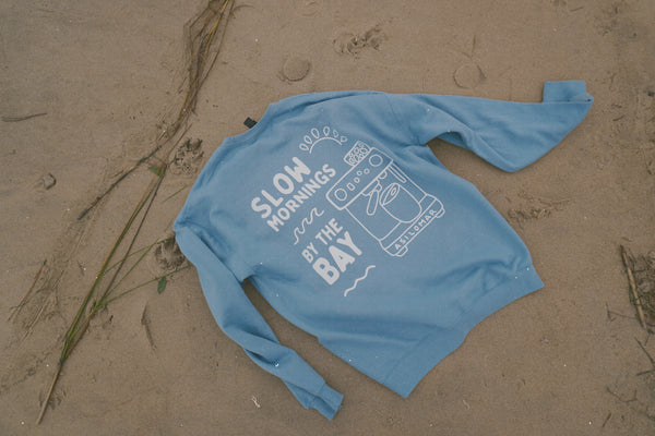 Blue long-sleeve shirt with text and graphics on a sandy surface