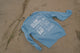 Blue long-sleeve shirt with text and graphics on a sandy surface