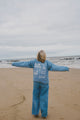 Person standing on a beach with arms outstretched, wearing a blue outfit with text.