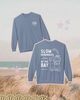 Blue sweatshirt with 'Slow Mornings by the Bay' text and graphics on a beach background