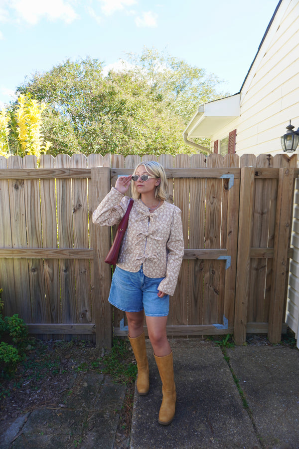 Woman standing in a backyard wearing a floral blouse, blue shorts, and yellow rain boots.