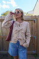 Woman wearing a floral jacket and sunglasses, standing in front of a wooden fence.