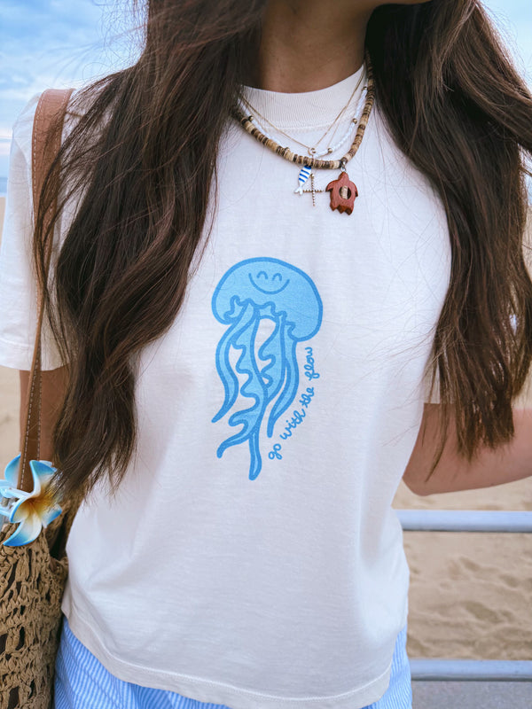 Person wearing a white t-shirt with a blue jellyfish design on a beach.