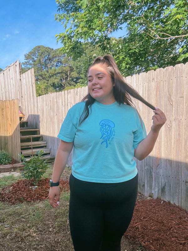 Person wearing a light blue t-shirt with a jellyfish design outdoors.