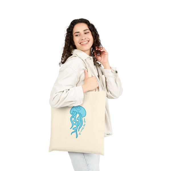 A person holding a beige cotton tote bag with a hand-drawn blue jellyfish design.
