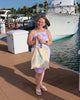 Woman holding a tote bag on a dock with boats in the background