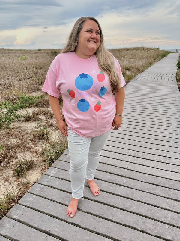 Woman wearing a pink t-shirt with colorful designs on a wooden boardwalk.