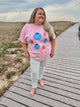 Woman wearing a pink t-shirt with colorful designs on a wooden boardwalk.