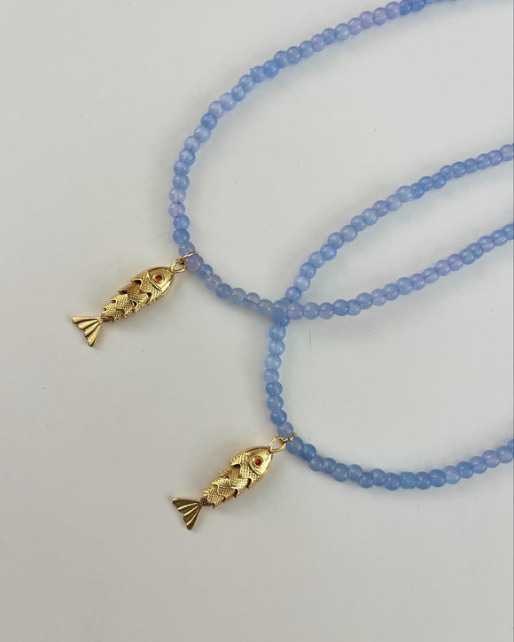 Two blue beaded necklaces with gold fish pendants on a light gray background