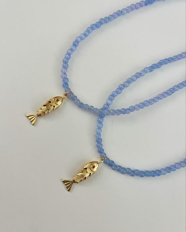 Two blue beaded necklaces with gold fish pendants on a light gray background