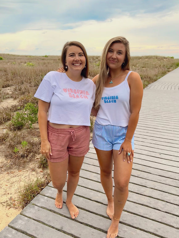 Two women standing on a wooden boardwalk at the beach, wearing matching t-shirts with 'Virginia Beach' text.