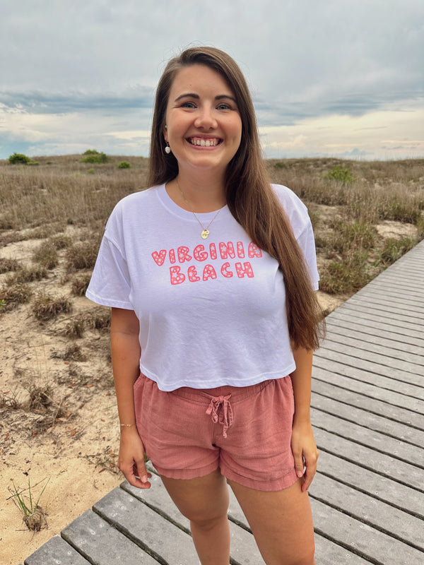 Woman wearing a 'Virginia Beach' t-shirt standing on a wooden boardwalk with a beach background.