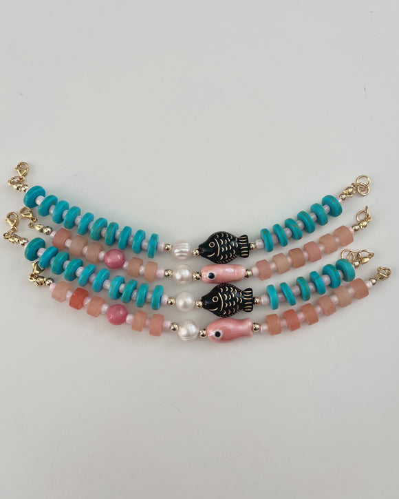 pink and blue beaded bracelets with small fish acrylic beads and freshwater pearls on a white table surface.