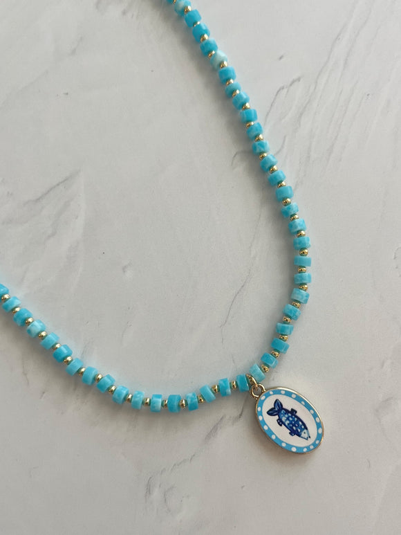 Turquoise beaded necklace with a blue fish pendant on a light gray background