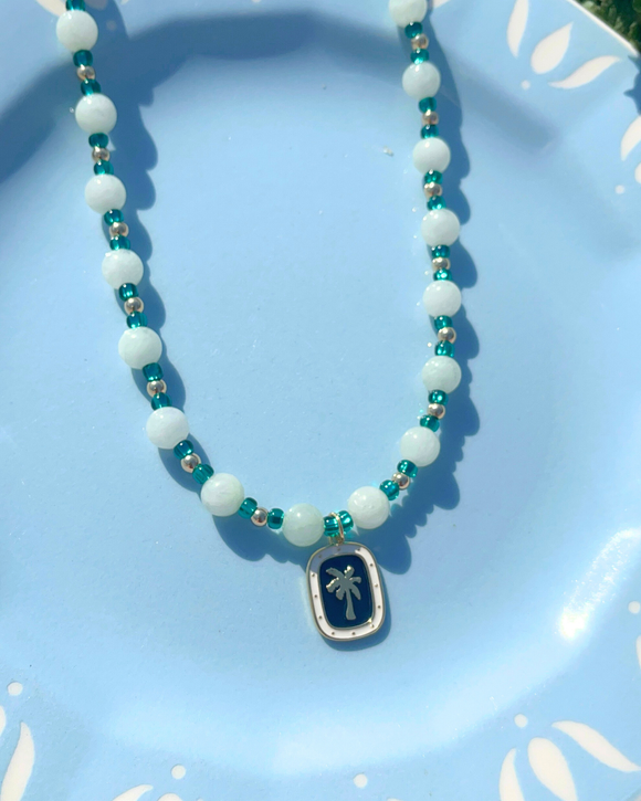 Necklace with white beads and a palm tree pendant on a light blue plate